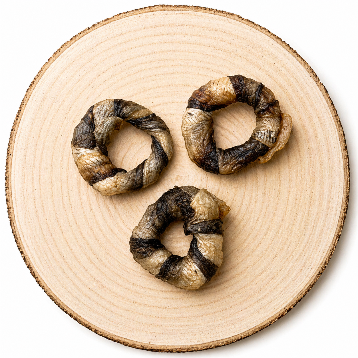 Three braided fish skin chew rings (“fish donuts”) arranged in a triangular layout on a natural wood slice, showing a mix of light and dark textures against a clean, neutral background.